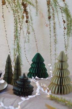 three green trees sitting on top of a table next to plates and cups with forks