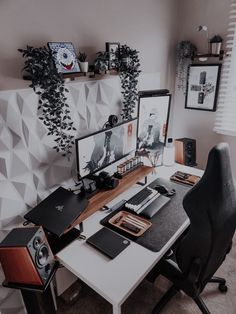 a computer desk with two monitors and speakers on it, in front of a wall decorated with plants