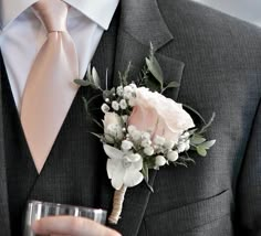 a man in a suit and tie holding a glass with flowers on it, while wearing a boutonniere