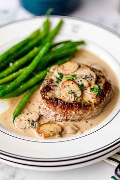 a white plate topped with meat covered in mushroom gravy and asparagus