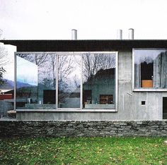 a concrete house with large windows and grass