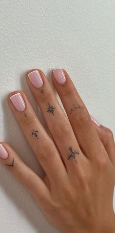 a woman's hand with some tattoos on her left thumb and fingers, holding onto a white wall