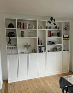 a living room with white bookcases and wooden floors