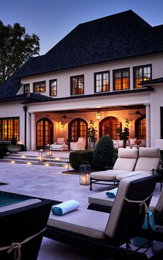 an outdoor patio with lounge chairs and candles lit up in front of a large house