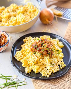 a black plate topped with macaroni and cheese next to a bowl of onions