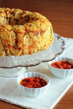 a bundt cake sitting on top of a glass plate next to bowls of sauce