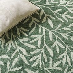 a green rug with white leaves on it and a pillow sitting on top of it