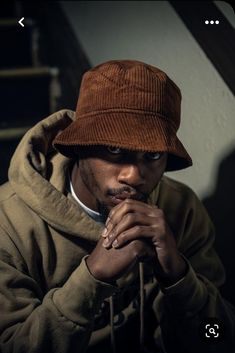 a man wearing a brown hat sitting on top of a stair case with his hands under his chin