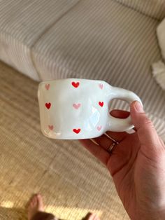 a hand holding a cup with hearts painted on it and sitting on the floor next to a bed