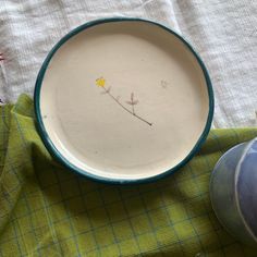 a white and blue plate sitting on top of a green table cloth next to a vase