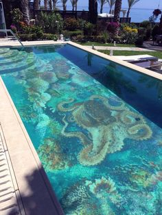 an outdoor swimming pool with blue water and colorful corals on the bottom edge, surrounded by palm trees