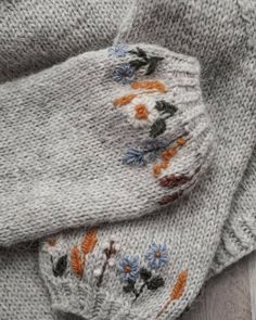 two knitted sweaters with flowers and leaves on them, one is grey and the other is white