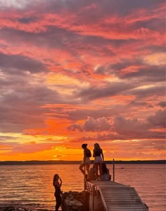 people standing on a dock watching the sun set