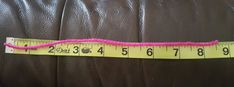 a measuring tape on the back of a brown leather couch with pink thread around it