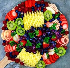 a platter filled with fruit and vegetables on top of a gray surface next to a wooden spatula