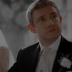 a man in a tuxedo looks off into the distance while wearing a flowered boutonniere