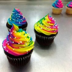 three cupcakes with rainbow frosting and sprinkles are on a table