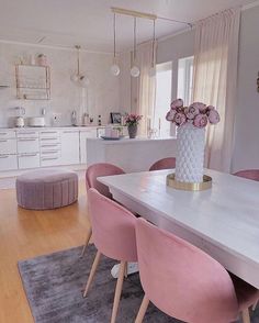 a dining room table with pink chairs and a white vase filled with flowers sitting on top of it