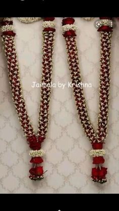 three red and white necklaces with flowers on them, hanging from the side of a wall