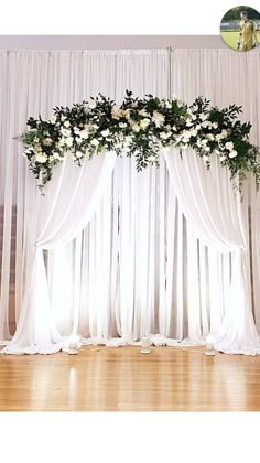 an arrangement of flowers and greenery on the back of a white drape curtain