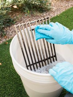 a person in blue gloves is cleaning a bucket with water and metal tongs on the grass