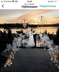 a bride and groom standing in front of a lake at sunset with candles on the ground