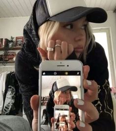 a woman taking a selfie with her cell phone while wearing a baseball cap and jeans