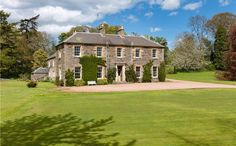 a large stone house in the middle of a lush green field