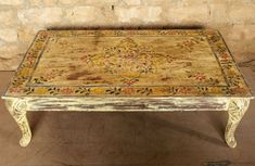 an old coffee table with a colorful rug on it's top sitting in front of a stone wall