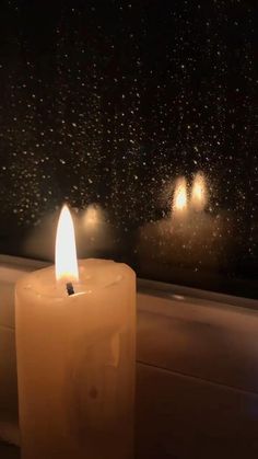 a lit candle sitting on top of a window sill in front of a rain covered window