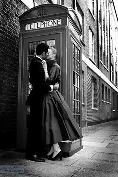 a man and woman kissing in front of a phone booth