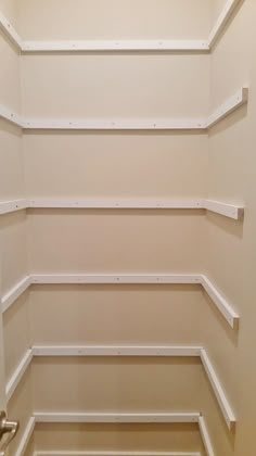 an empty closet with white shelving and wood flooring on the bottom half of it