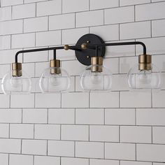 three clear glass globe lights hang from a black metal fixture on a white brick wall