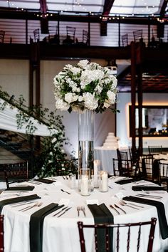 a tall vase filled with white flowers sitting on top of a table covered in black and white cloths