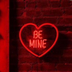 a neon sign that says be mine on a brick wall in the shape of a heart