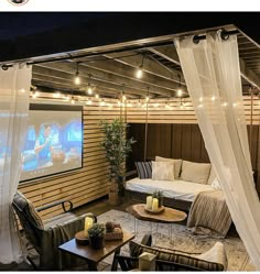 an outdoor living area with curtains, couches and a flat screen tv on the wall