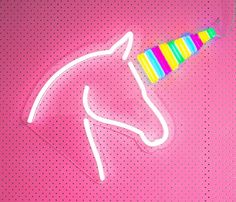 a neon unicorn head with a party hat on it's head, against a pink background