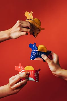 four hands holding small toy animals in front of red background with other hand reaching for them