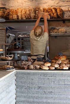 a woman reaching up to grab some bread from the counter at a bakery shop with lots of pastries on display