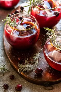 three glasses filled with red liquid and garnished with herbs on a wooden platter