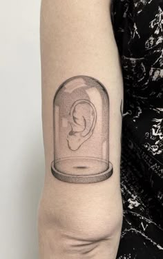 a woman's arm with a tattoo on it that has an image of a human ear in a glass jar