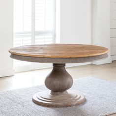 a round wooden table sitting on top of a rug in front of a white wall