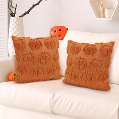 two decorative pillows on a white couch in front of a halloween tree and an orange pumpkin