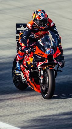 a man riding on the back of a motorcycle down a race track in an orange and black outfit