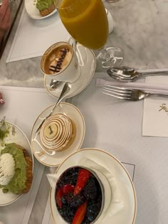 a table topped with plates and bowls filled with food next to glasses of orange juice