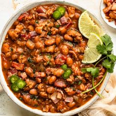 a white bowl filled with chili and beans next to a lime slice on the side