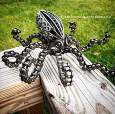 a metal spider sculpture sitting on top of a wooden bench in front of green grass