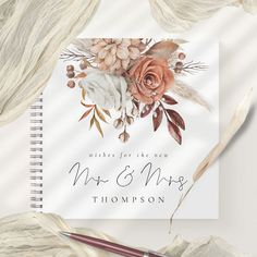 a wedding card with flowers and feathers on it, next to a pen and paper