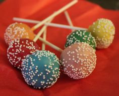 four cake pops with white sprinkles on red paper and wooden sticks sticking out of them