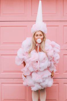 a woman in a pink fluffy dress and white hat standing next to a pink garage door